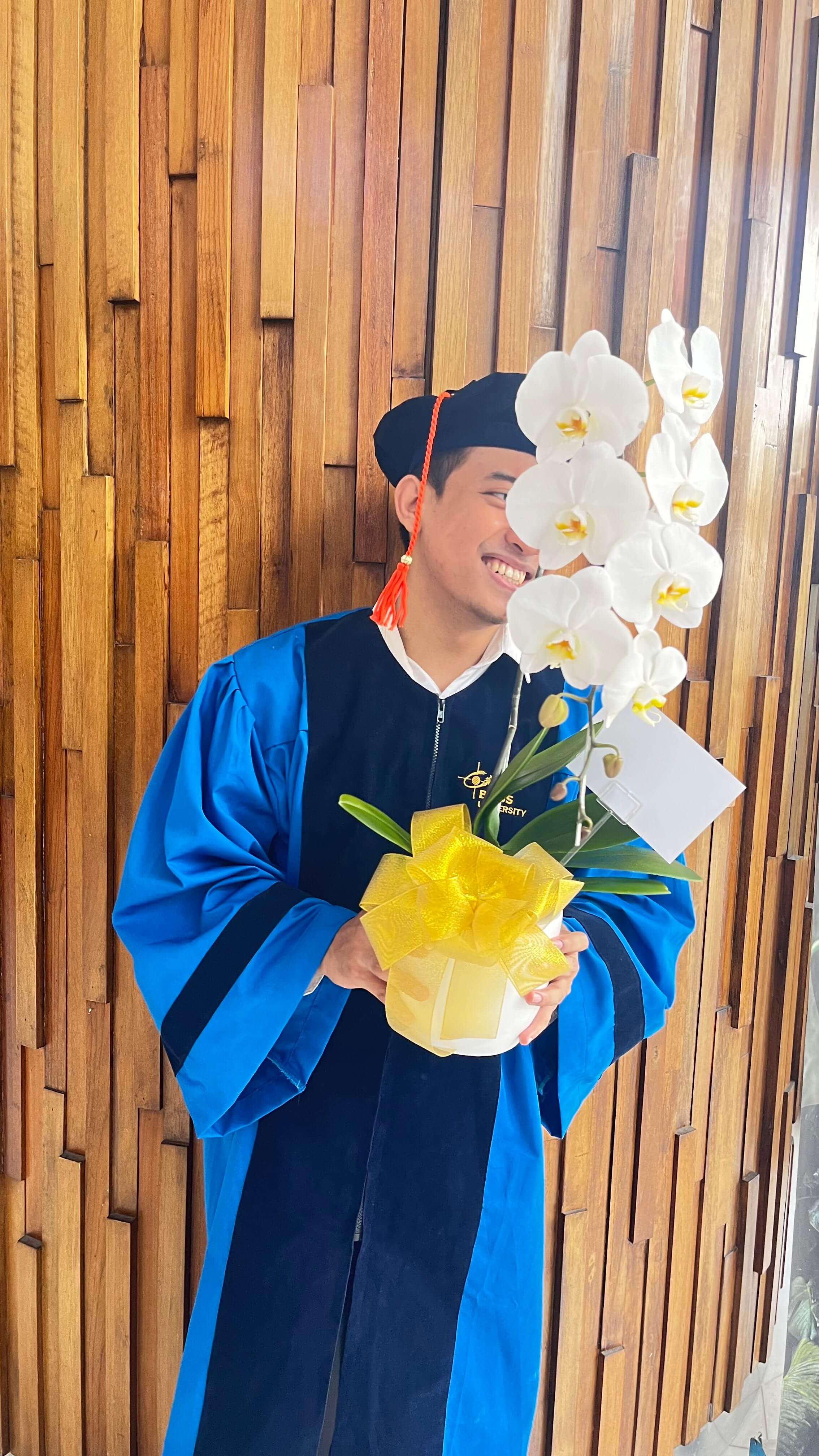Imam Abdul Aziz in a graduation gown holding flowers at Binus University